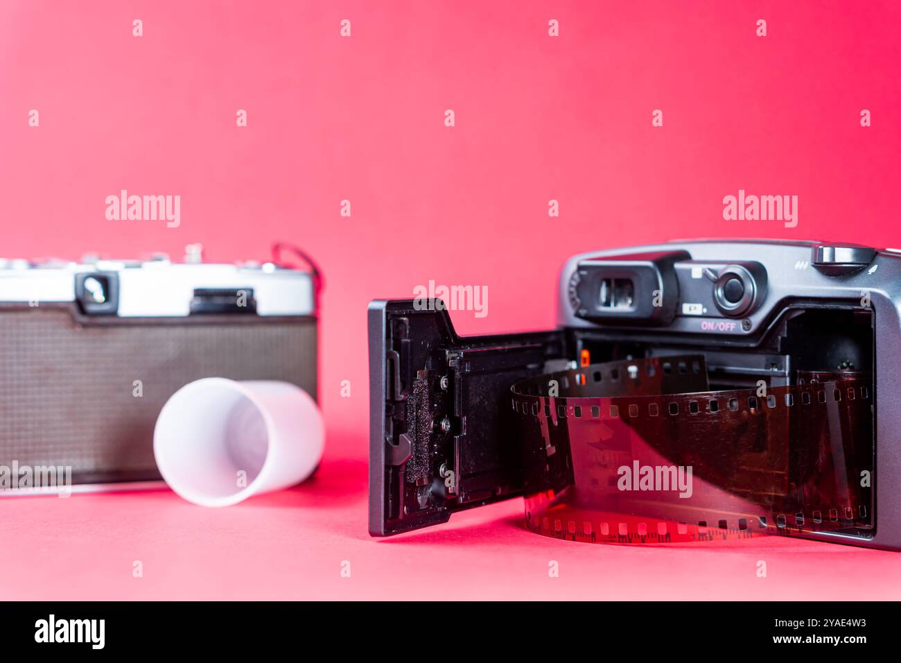 Una macchina fotografica vintage con scomparto aperto per la pellicola, che rivela un rotolo di pellicola. Sullo sfondo, c'è una vecchia macchina fotografica e una tazza bianca. Il bac Foto Stock