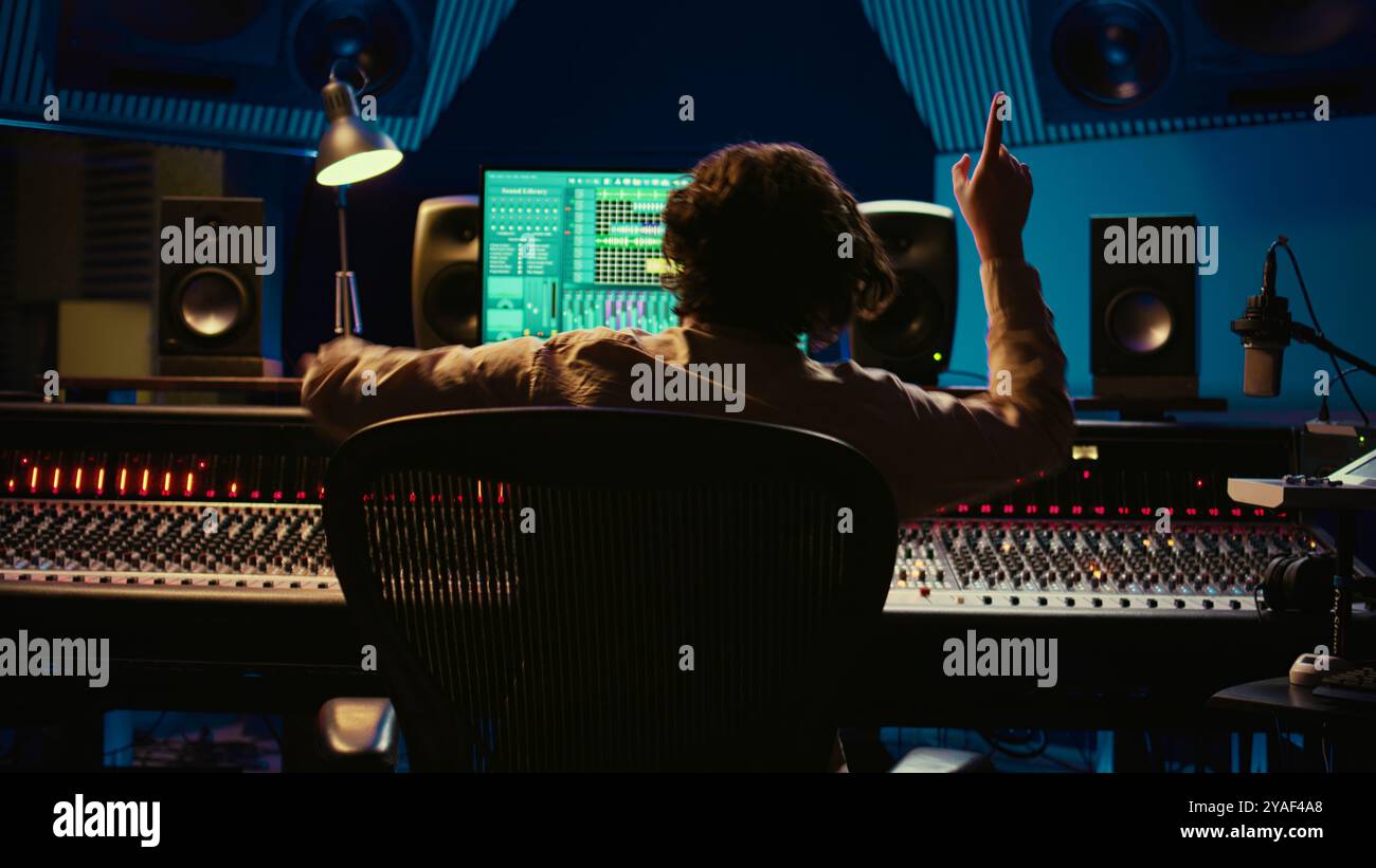 Allegro ingegnere del suono che balla sulla sua creazione musicale in studio professionale, modifica una registrazione su console di missaggio e software daw. Sound designer elabora i brani. Telecamera B.. Foto Stock