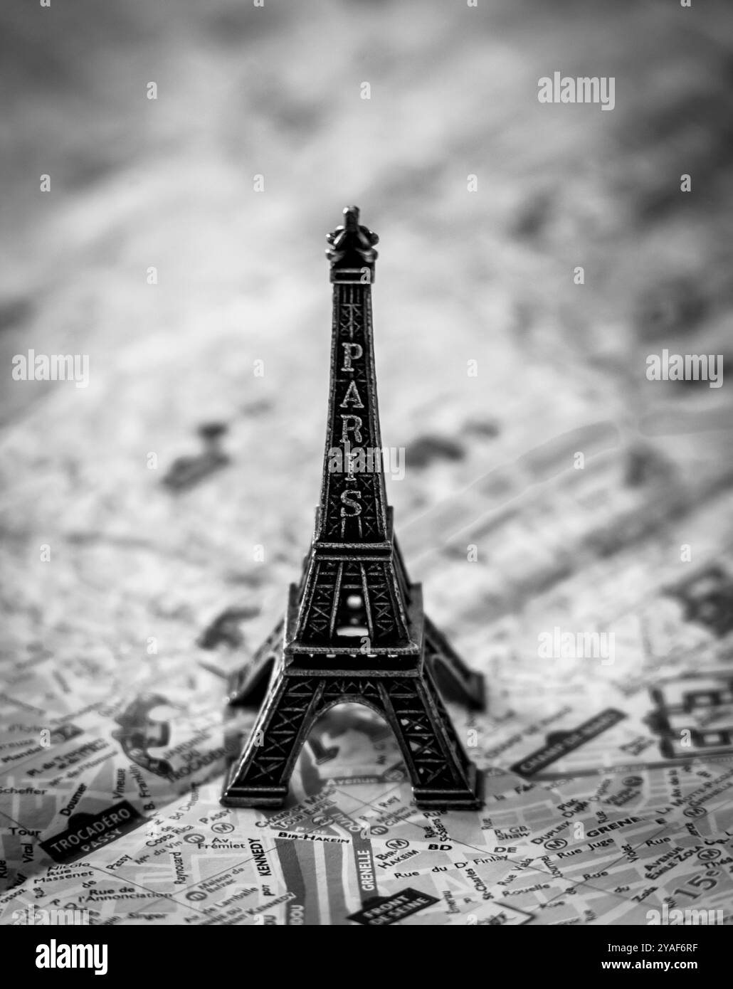 Una replica in miniatura in metallo della Torre Eiffel incombe sulla cartina stradale di Parigi per illustrazioni e divertimento in bianco e nero Foto Stock
