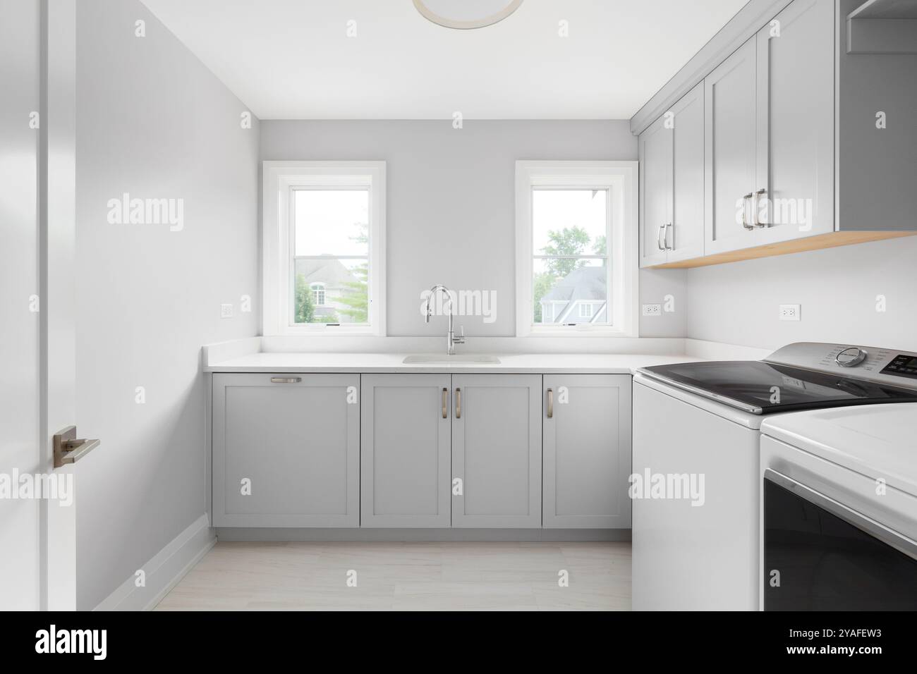 Una lavanderia con armadi grigi, ripiani in marmo bianco, lavatrice e asciugatrice bianche e pavimento piastrellato marrone. Nessun marchio o etichetta. Foto Stock