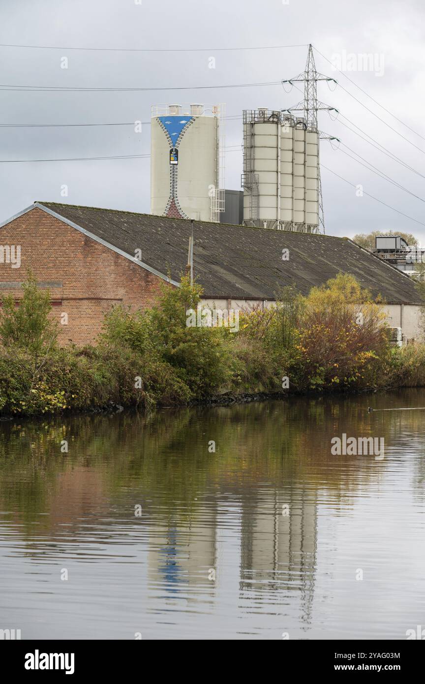 Gijzegem, regione fiamminga orientale, 11 04 2022, silo industriale e stoccaggio di massa che si riflettono nell'acqua del fiume Dender Foto Stock