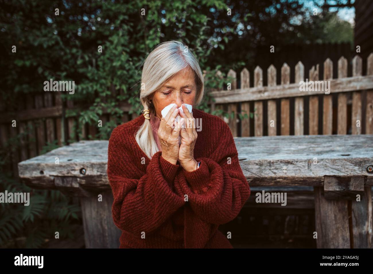 Una donna anziana si sente male, soffiando il naso che cola e soffice nel tessuto e starnuto. Foto Stock