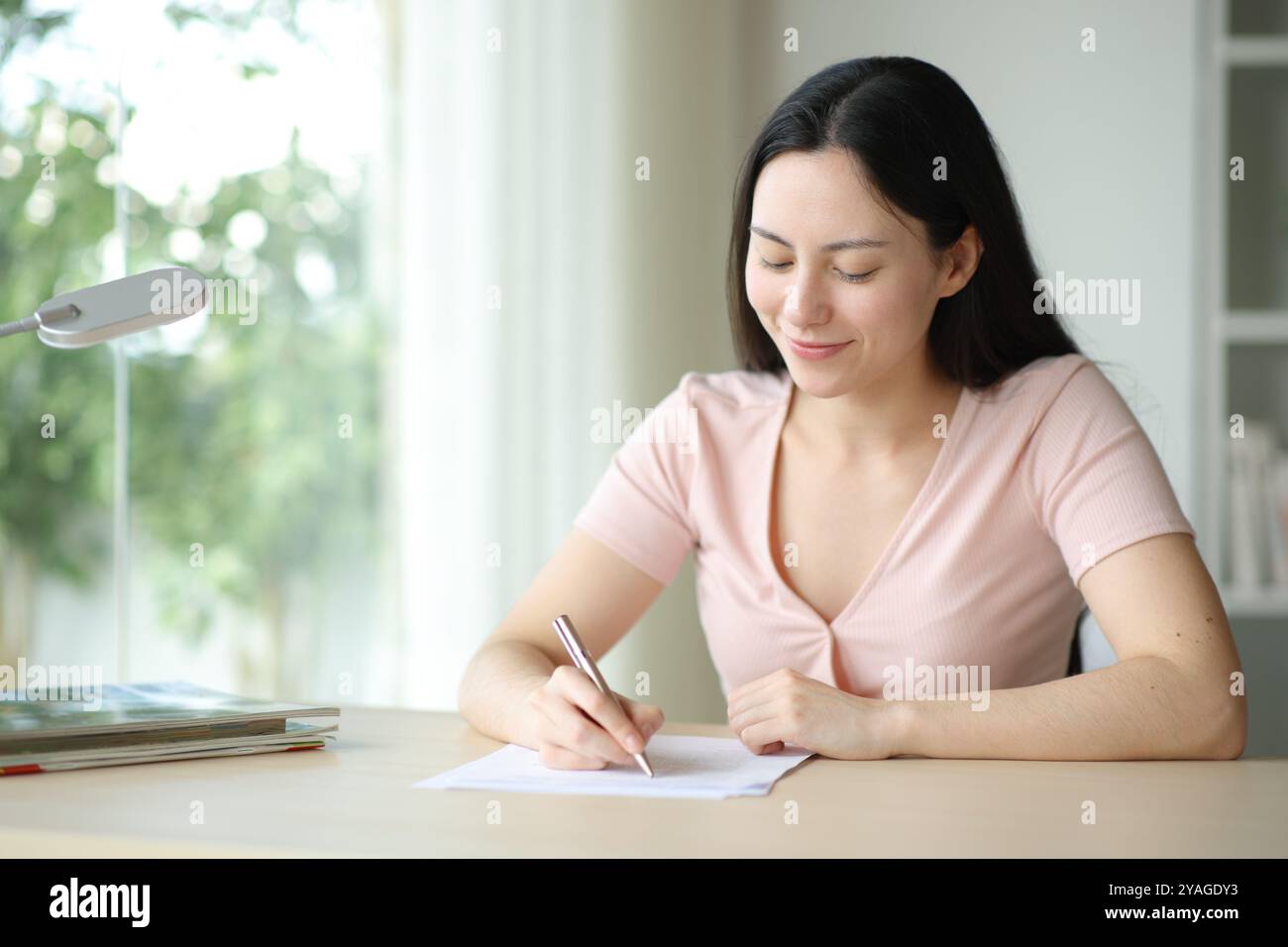 Donna asiatica che compila il modulo o firma il contratto in una scrivania a casa Foto Stock