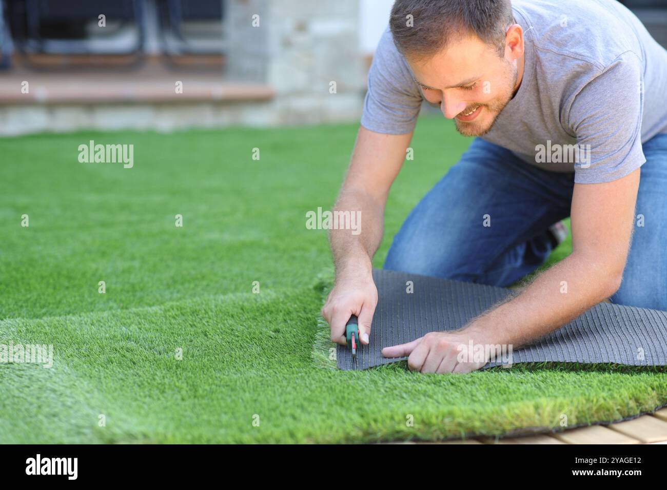 Uomo felice che installa un prato artificiale che taglia un pezzo nel giardino di casa Foto Stock