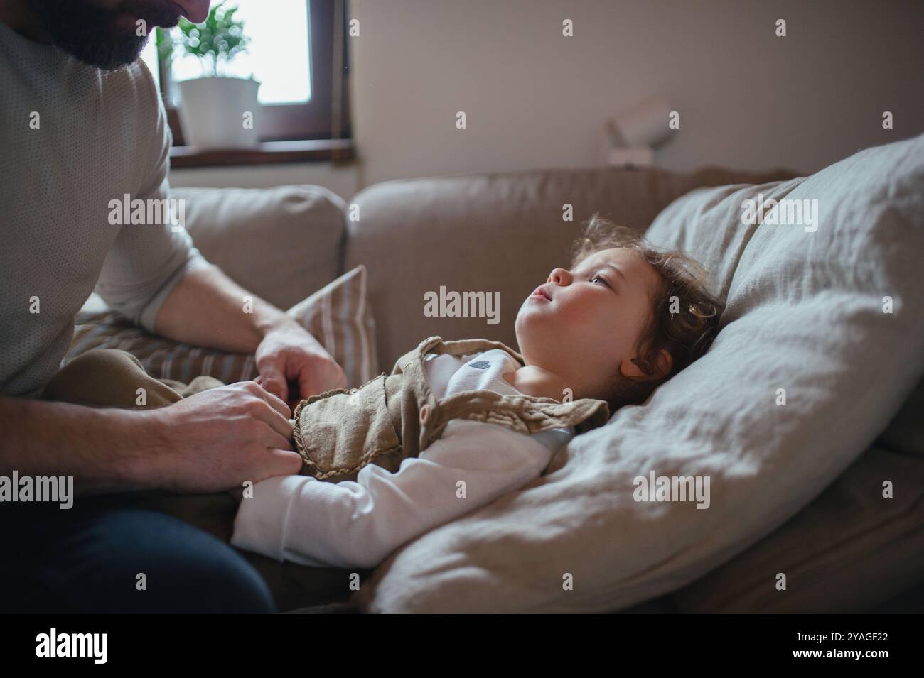 Padre che si prende cura di una ragazza malata con febbre e freddo a casa. Figlia sdraiata sul divano, si sente stanca. Foto Stock