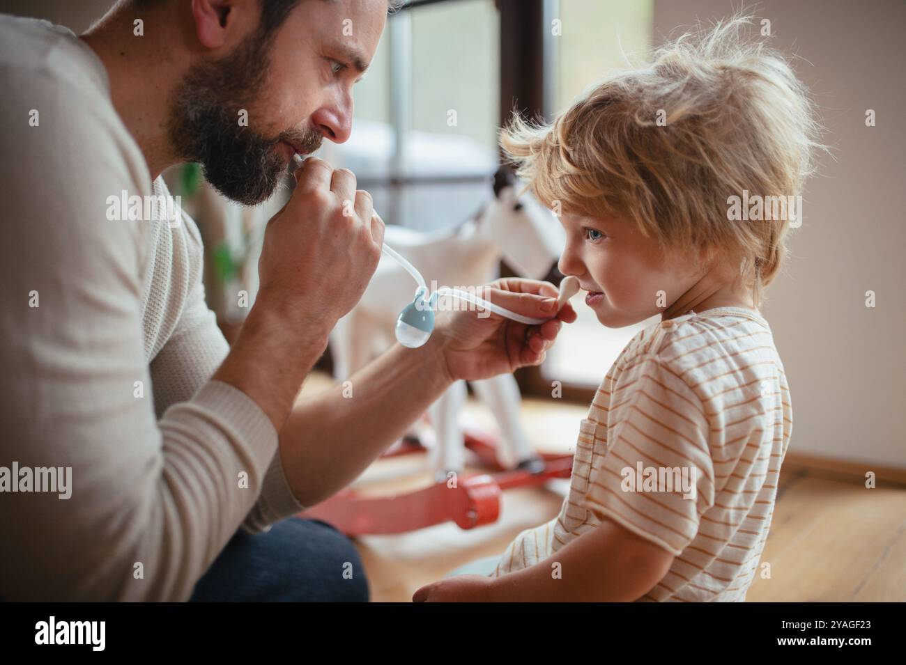 Padre che aiuta il figlio con il naso chiuso, che usa una lampadina nasale per eliminare il muco dal naso. Foto Stock