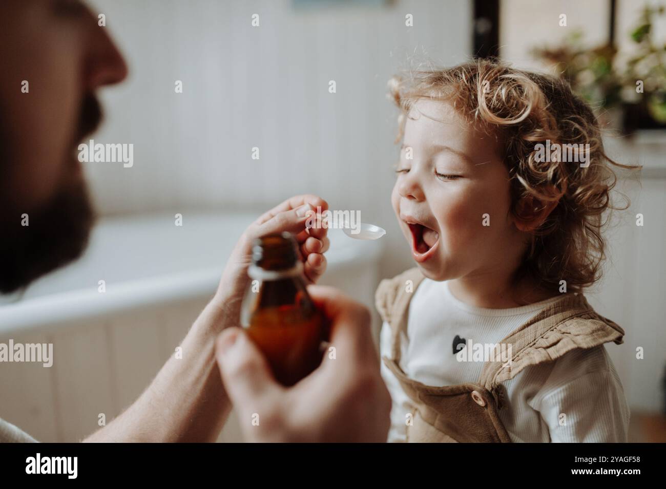 Ragazza malata con febbre e freddo a casa. Padre che dava alla figlia medicine su cucchiaio, sciroppo per tosse o medicina per la febbre. Foto Stock