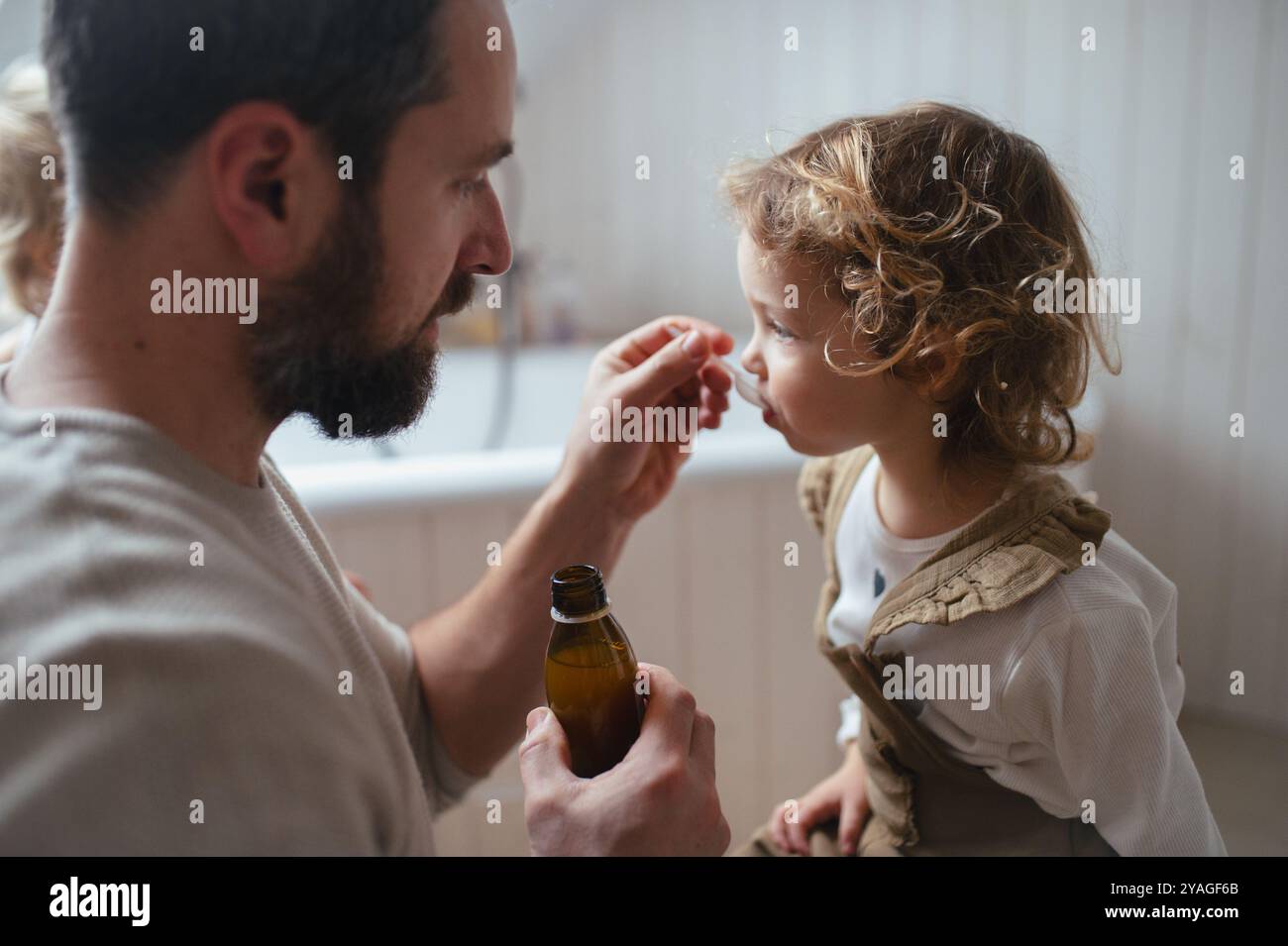Ragazza malata con febbre e freddo a casa. Padre che dava alla figlia medicine su cucchiaio, sciroppo per tosse o medicina per la febbre. Foto Stock