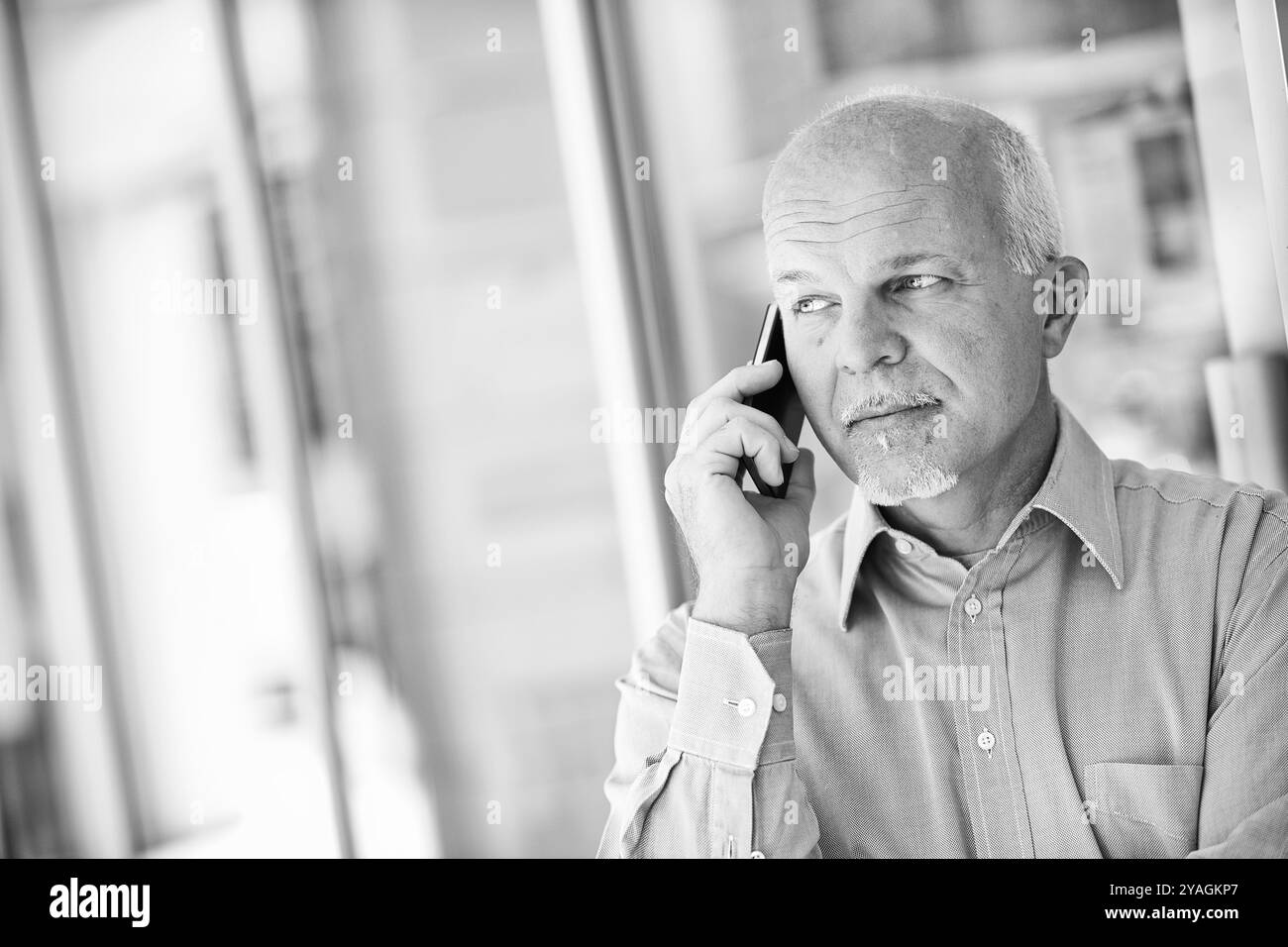 Uomo d'affari maturo in un ufficio moderno, impegnato in una telefonata, trasuda fiducia e attenzione. Immagine monocromatica con ampio spazio di copia f Foto Stock