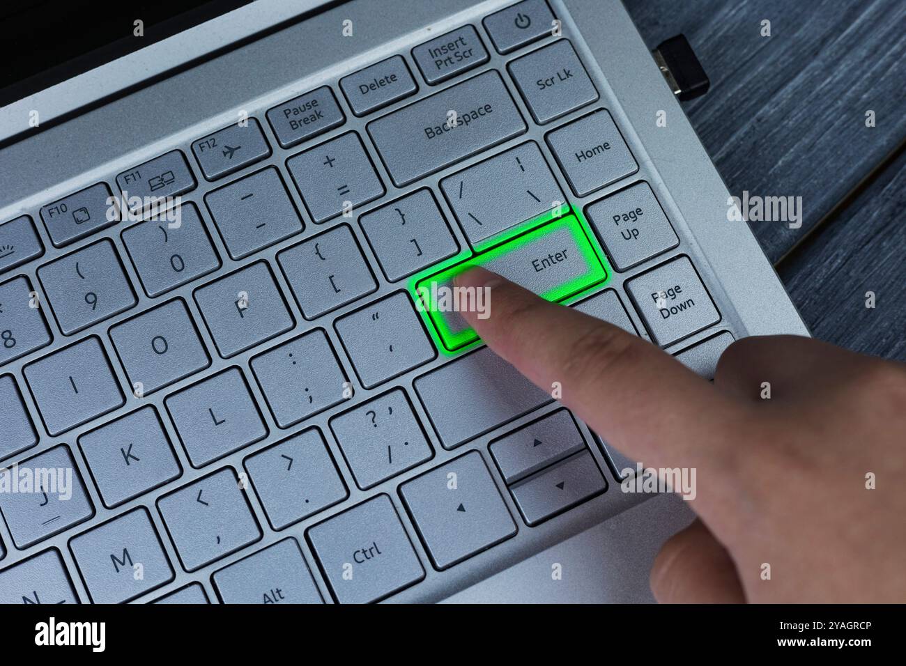Una persona sta premendo attivamente un pulsante verde brillante situato sulla tastiera di un notebook, completamente concentrato sul proprio compito Foto Stock