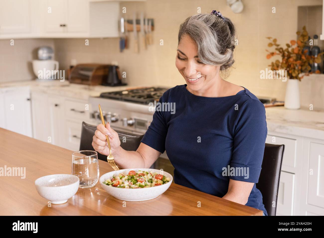 Donna che sorride alla sua Macedonia di frutta in cucina Foto Stock