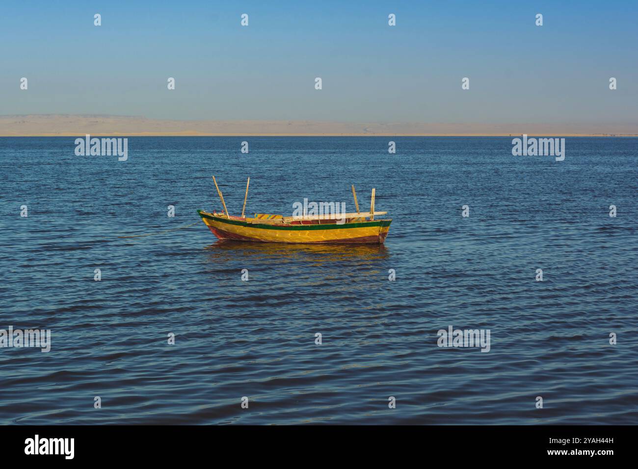 Una piccola barca colorata che si allontana su un mare calmo contro il cielo blu Foto Stock