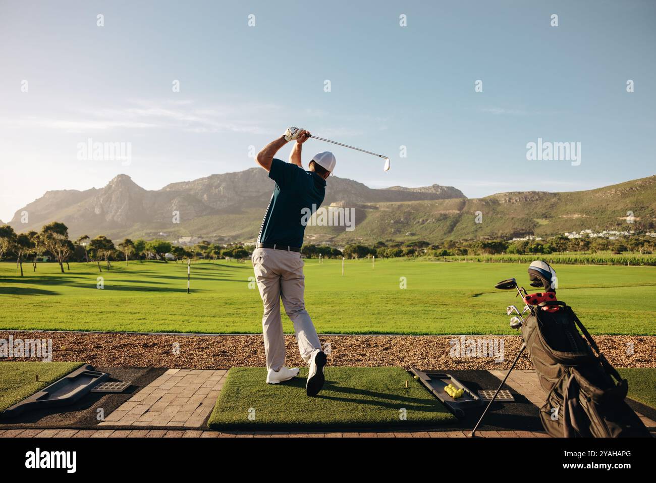 Golfista maschile che gioca su un bellissimo campo di montagna in un centro di golf, la sua borsa da golf si trova nelle vicinanze. Perfetto per gli amanti del golf e della natura Foto Stock