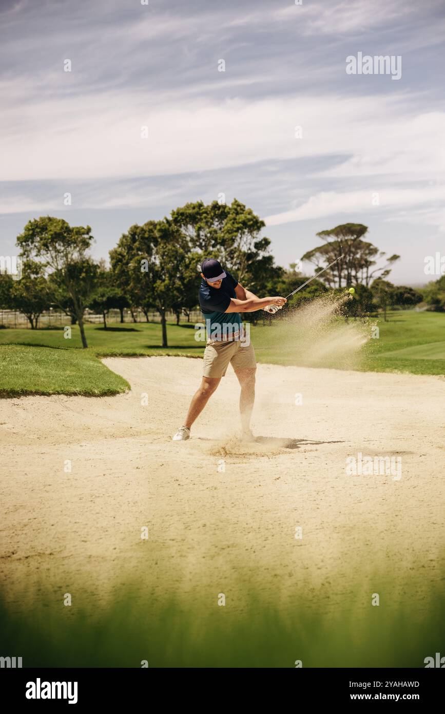 Golfista maschile che esegue un colpo di sabbia con follow-through su un campo soleggiato, illustrando abilità e precisione in una partita competitiva. Foto Stock
