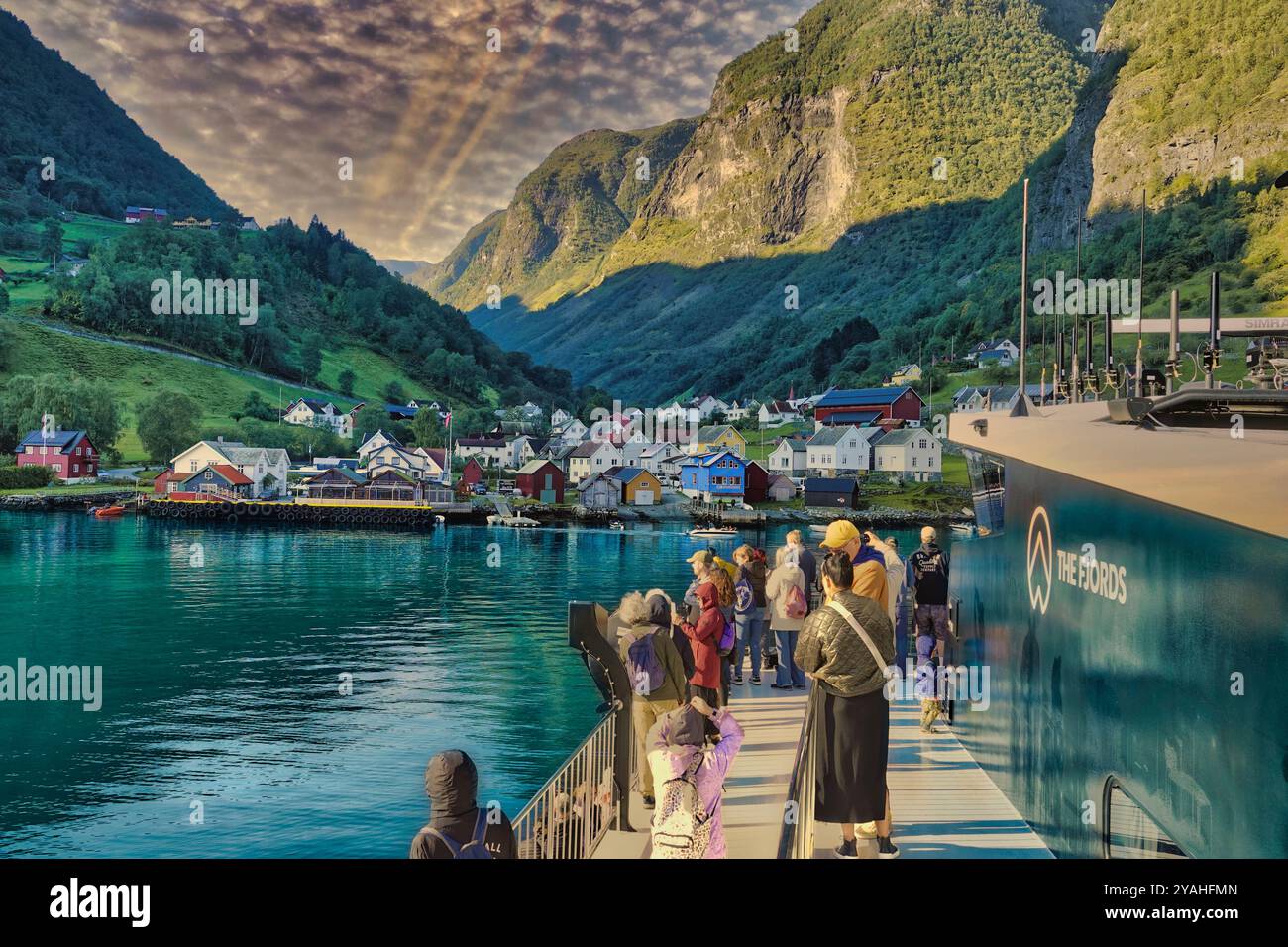 7 settembre, 2024 Flam & Bergen, Norvegia Vista del colorato villaggio Undredal sotto spettacolari nuvole mattutine, i turisti aspettano di attraccare e lasciare il porto Foto Stock