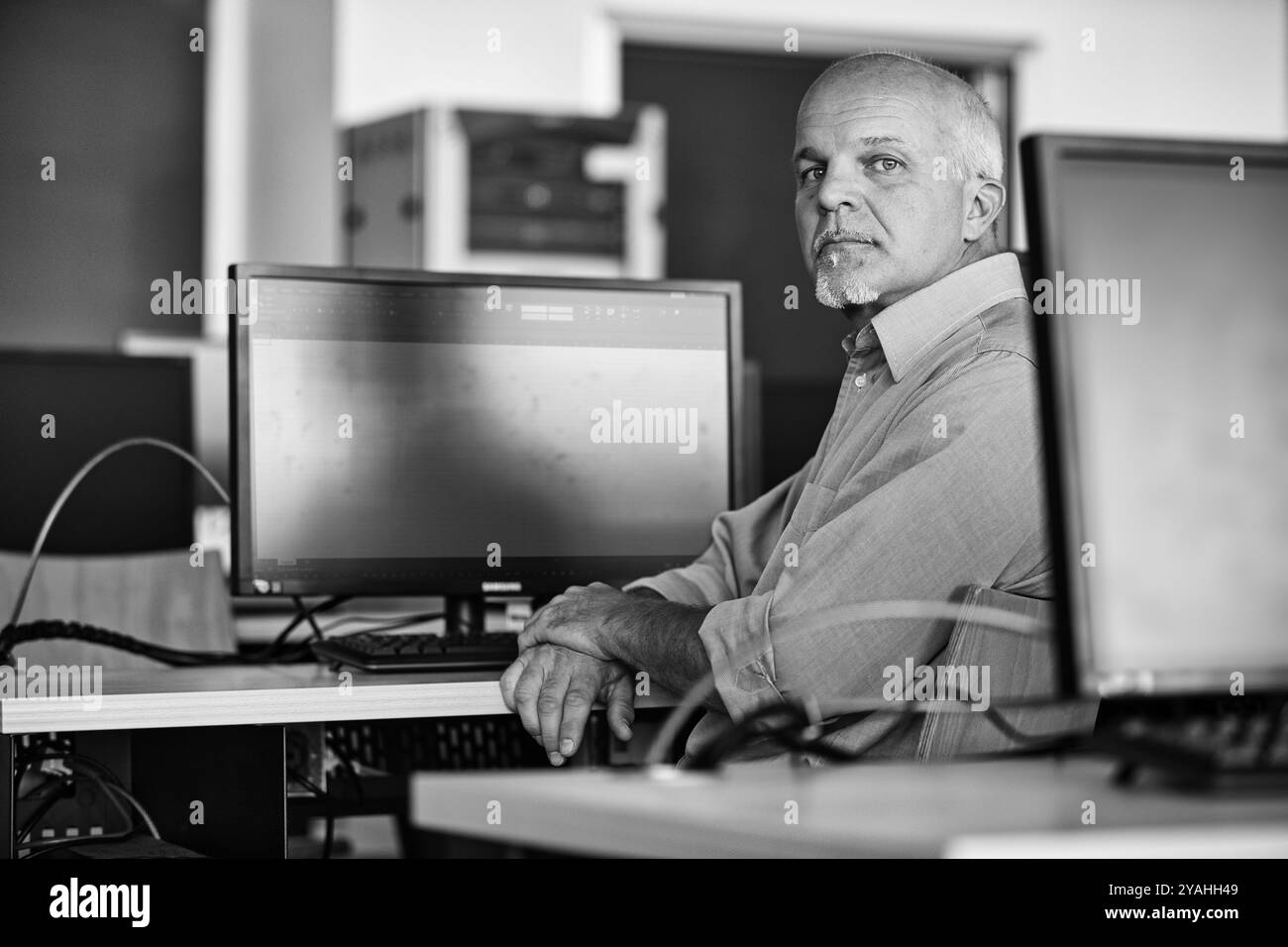 Uomo maturo che lavora su un computer in un ufficio moderno, con un aspetto serio e sicuro di sé. Adatto per concetti aziendali, tecnologici e didattici Foto Stock