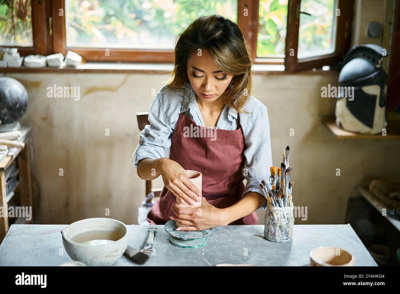 L'artista donna scolpisce i mestieri con l'argilla ceramica nel suo laboratorio creativo. Padroneggia l'arte della ceramica artigianale Foto Stock