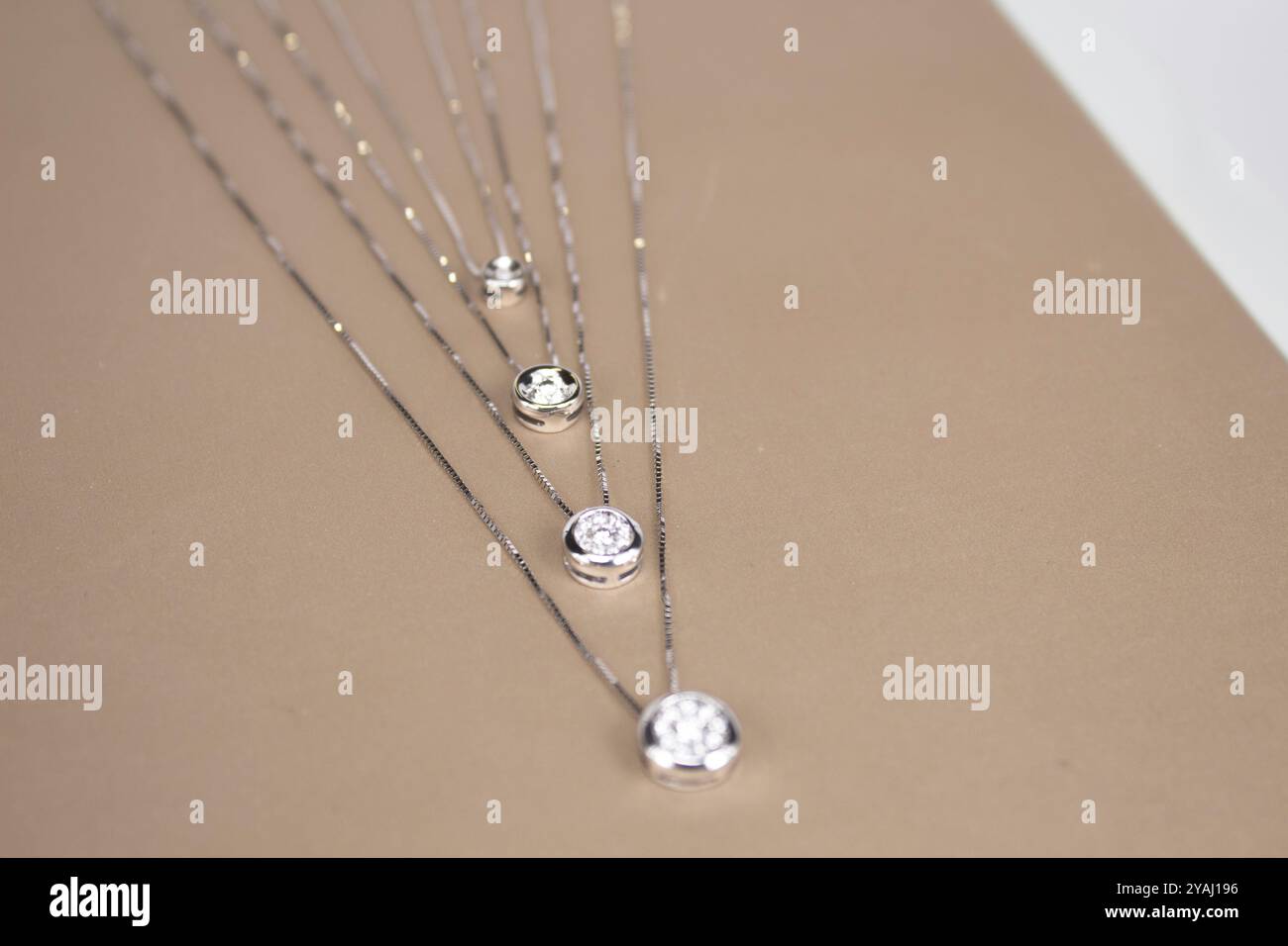 collezione di delicate collane in oro con pendenti rotondi in pietra preziosa con lunetta disposti in ordine decrescente per dimensioni su sfondo beige Foto Stock