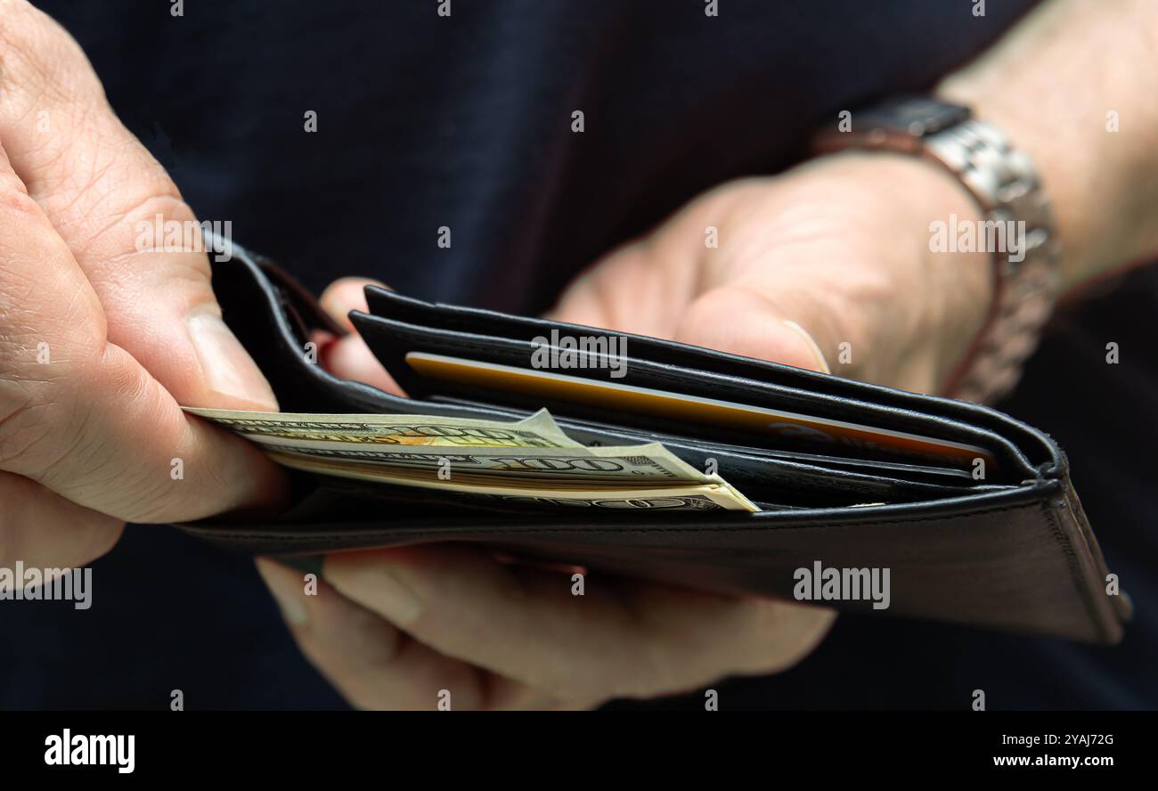Primo piano di una persona che apre un portafoglio, rivela contanti e carte di credito, simboleggia la finanza e le spese personali. Foto Stock