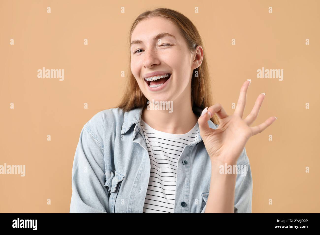 Ragazza sorridente con apparecchi che mostrano un gesto discreto su sfondo beige Foto Stock