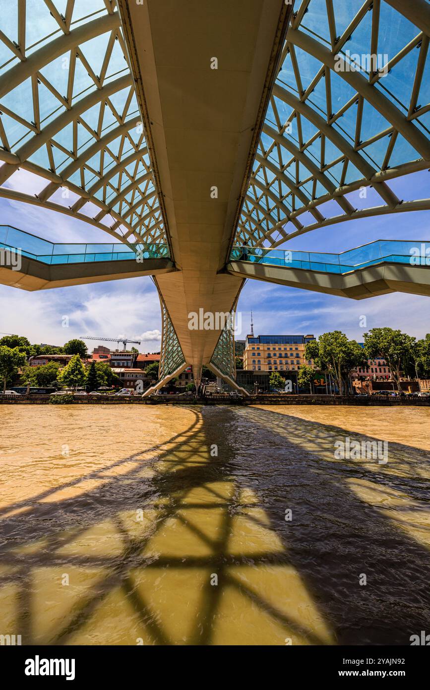 guardando verso l'alto la tettoia di vetro, la passerella pedonale e le scale dell'iconico ponte della pace e le ombre sul fiume kura tbilisi georgia Foto Stock