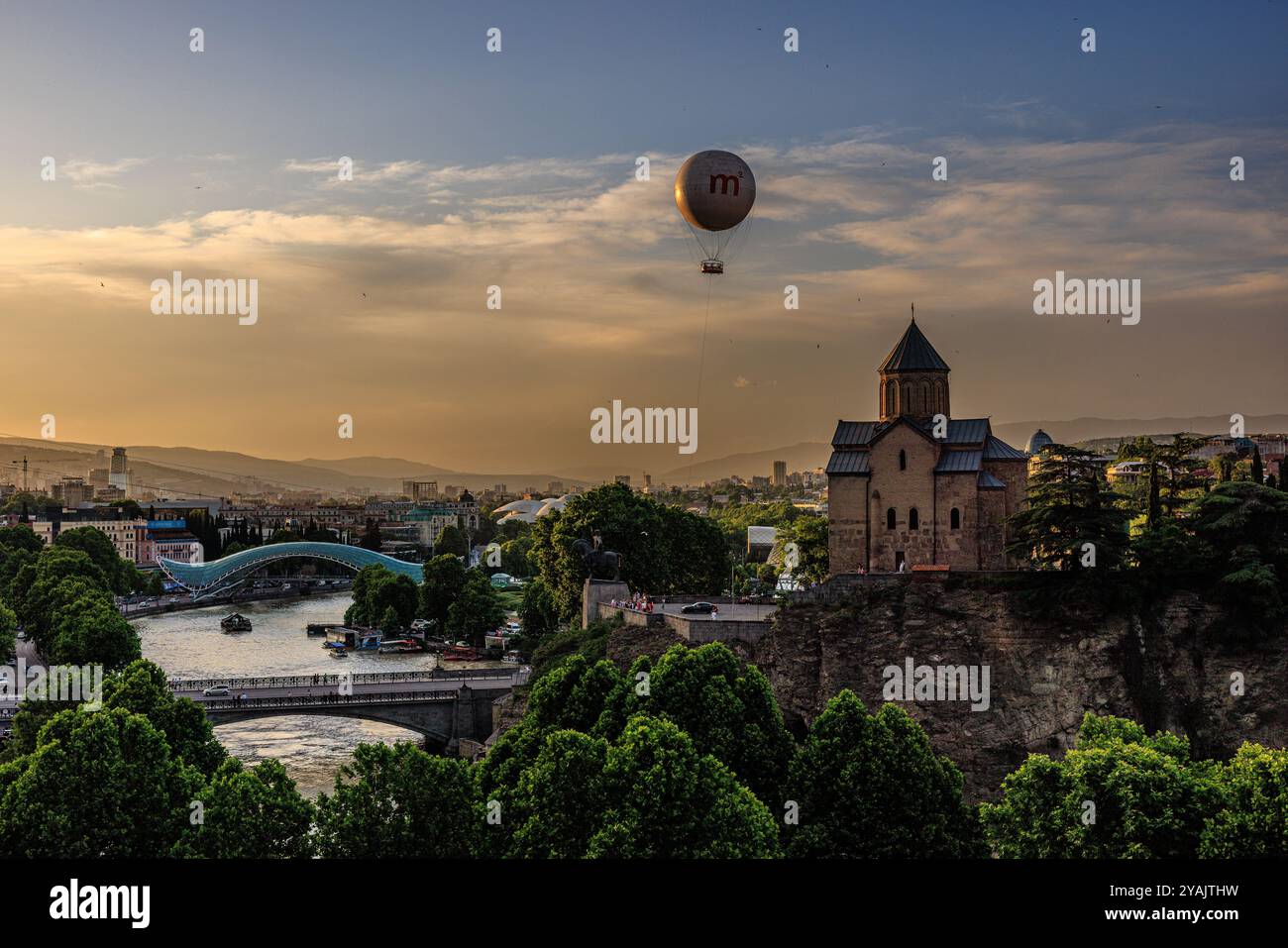 vista serale di tbilisi al tramonto mentre la mongolfiera guarda in basso sul ponte della pace e sul fiume kura con la chiesa di metekhi arroccata in cima alla scogliera Foto Stock