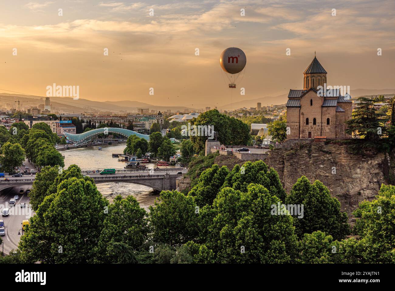vista serale di tbilisi al tramonto mentre la mongolfiera guarda in basso sul ponte della pace e sul fiume kura con la chiesa di metekhi arroccata in cima alla scogliera Foto Stock