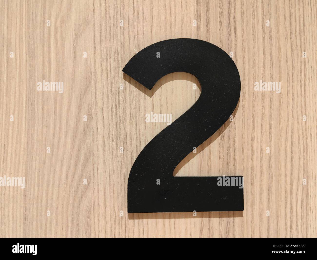 Segno minimalista: Numero 2 nero su parete marrone in legno con spazio negativo in un camerino Foto Stock