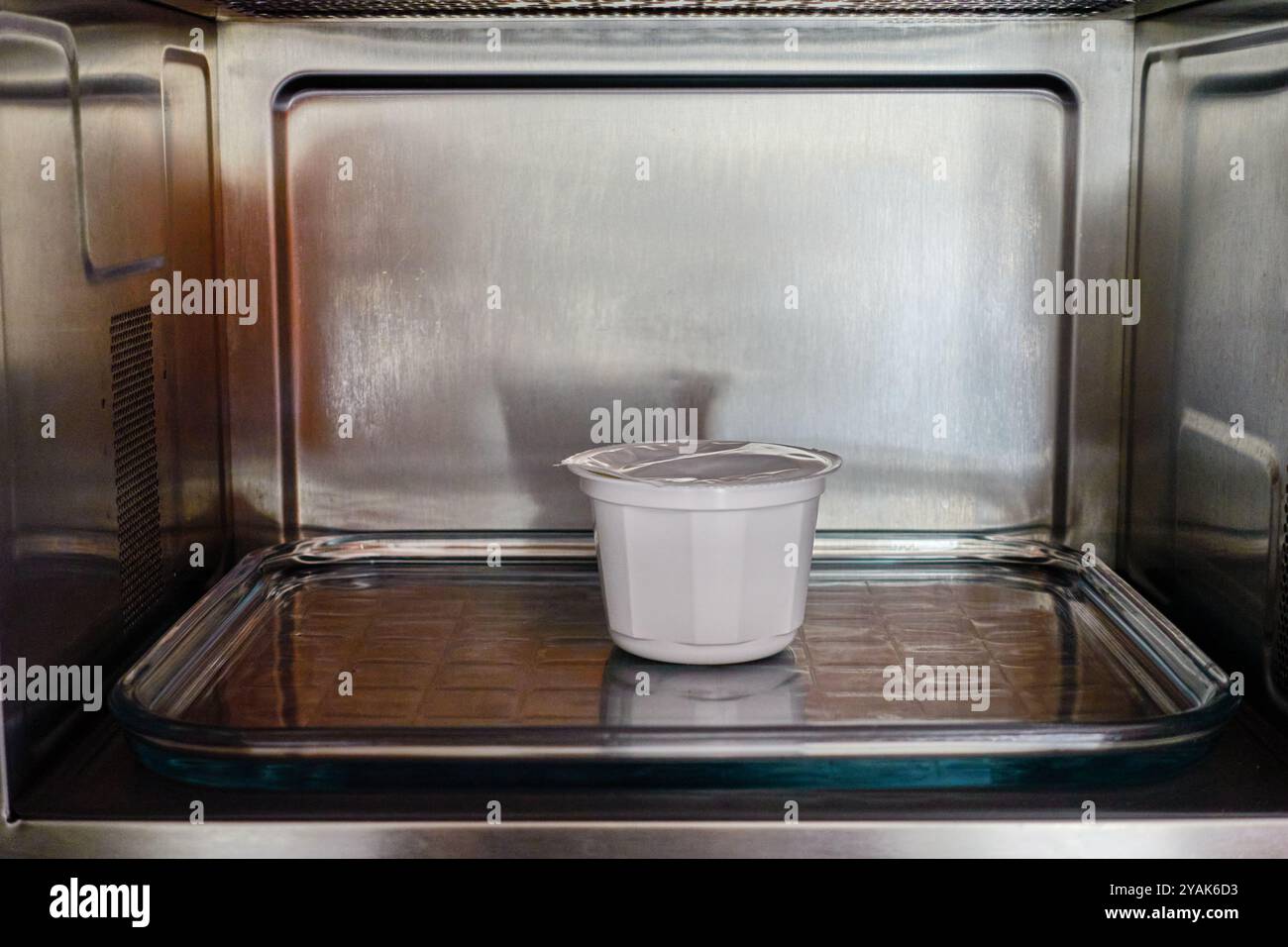 Un piccolo contenitore di plastica bianca su un vassoio di vetro all'interno di un forno a microonde predisposto per riscaldare e preparare un pasto Foto Stock