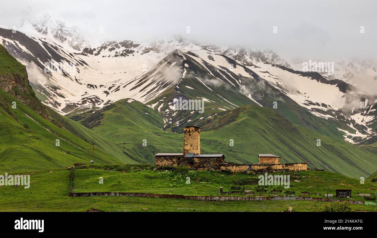 una delle torri difensive del remoto villaggio di montagna ushguli si trova su una collina verde di fronte alle montagne innevate dell'alta svaneti Foto Stock