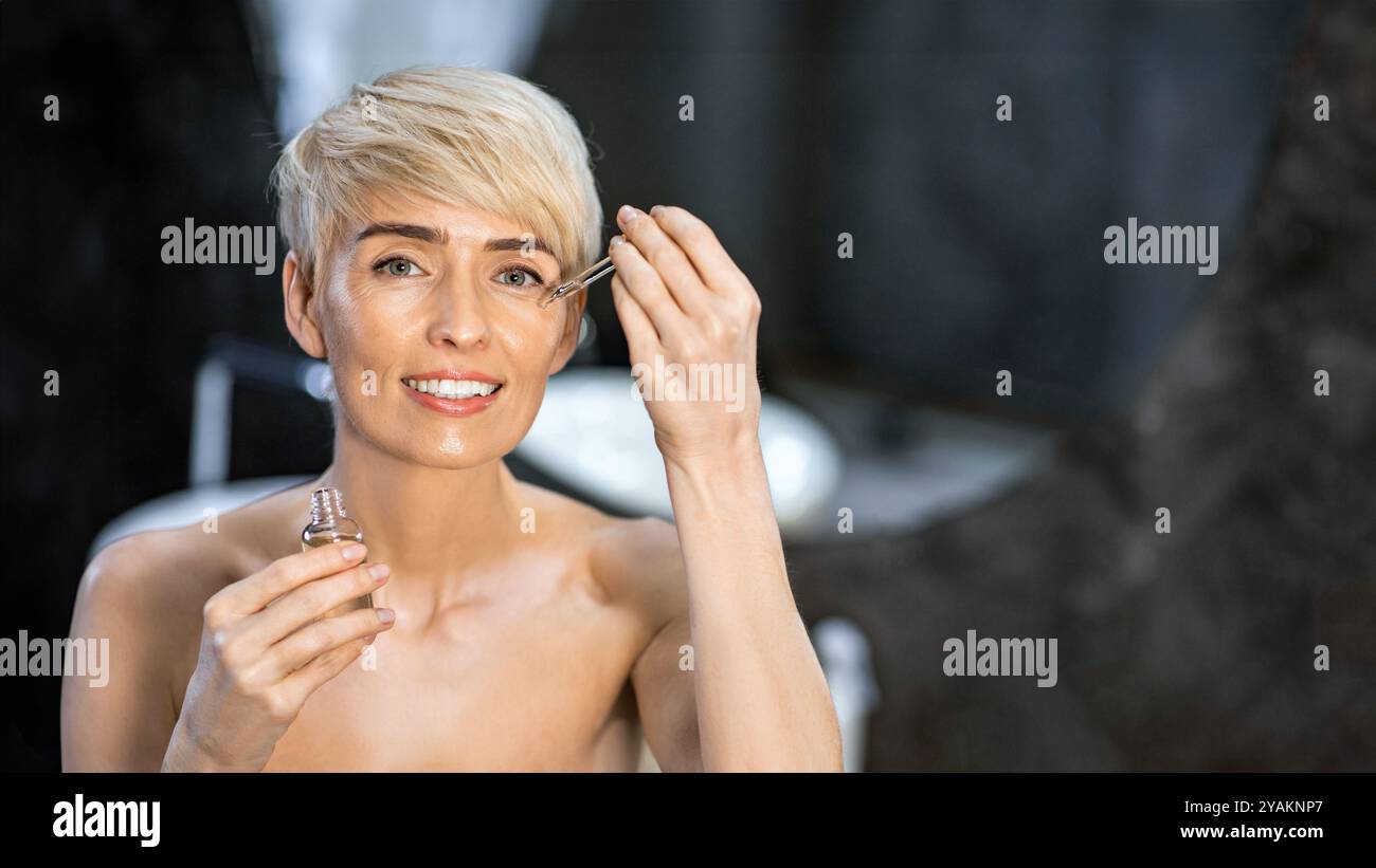 Donna con contagocce che applica olio cosmetico in bagno a casa Foto Stock