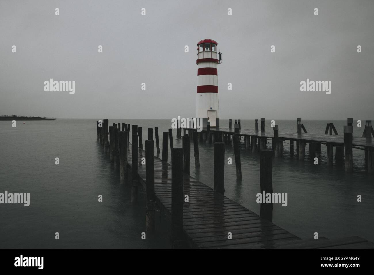 Un faro alla fine di un molo di legno sotto un cielo grigio su acque calme, Podersdorf, Burgenland, Austria, Europa Foto Stock