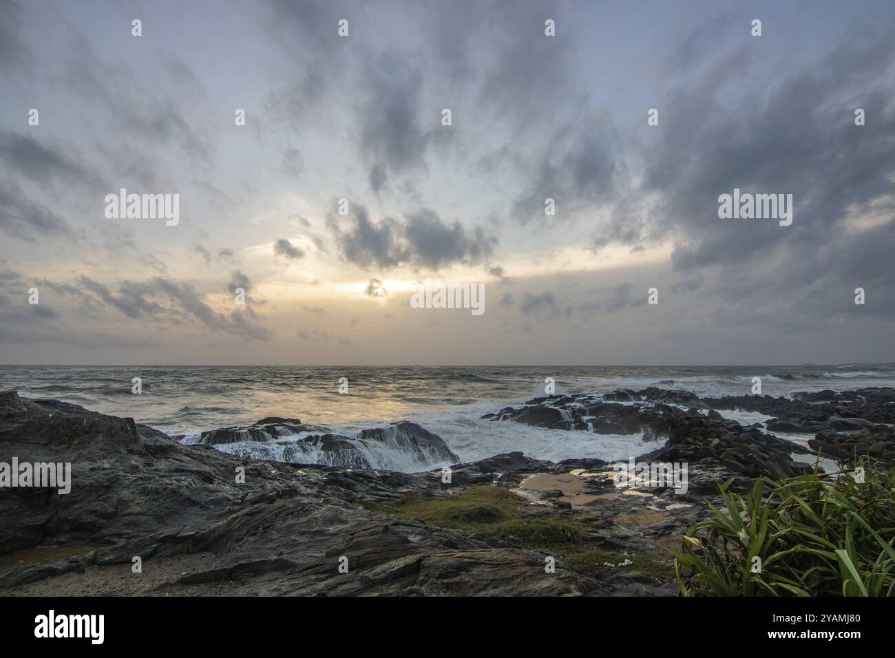 Spiaggia, con rocce laviche e vegetazione, vista sul mare la sera al tramonto. Paesaggio con nuvole a Induruwa, Bentota Beach, Sri Lanka, India, A. Foto Stock