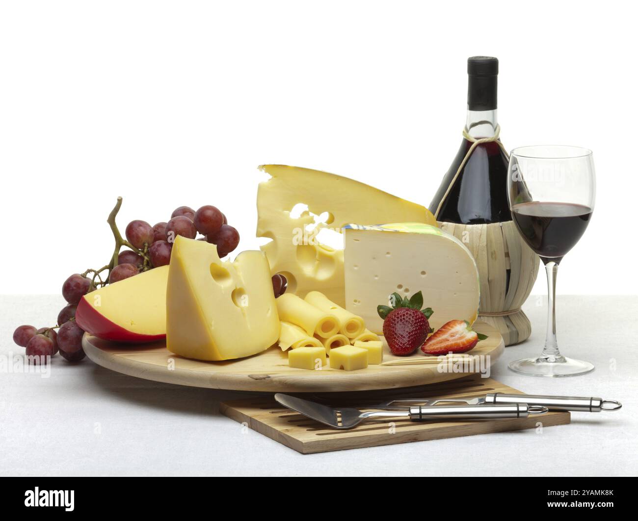 Composizione di formaggio, uva, bottiglie e bicchieri di vino e fragole su un vassoio rotondo di legno su una tovaglia bianca, isolato su uno sfondo bianco Foto Stock