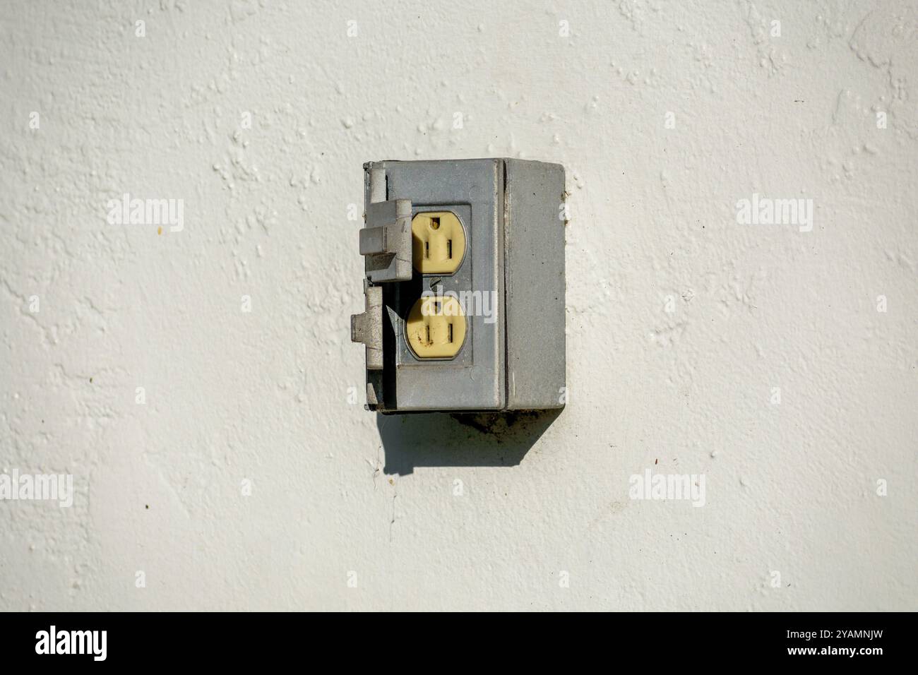 Una scatola di presa elettrica in metallo per esterni montata su una parete bianca testurizzata che mostra segni di usura. Foto Stock