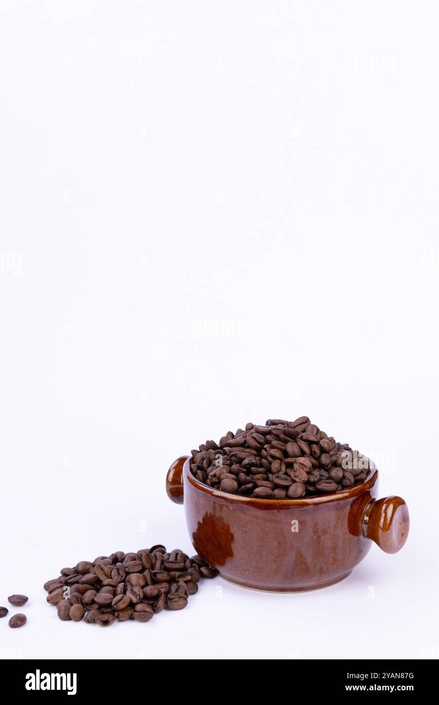 Una ciotola marrone splendidamente disposta piena di chicchi di caffè aromatici, con chicchi aggiuntivi disposti ad arte su uno sfondo bianco Foto Stock