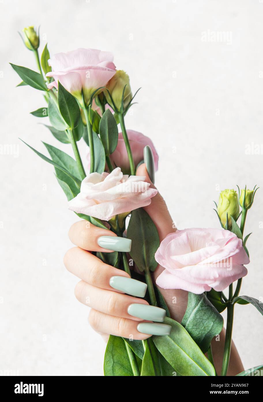 Una mano sottile mostra lunghe unghie color pastello mentre afferra delicatamente un bouquet di fiori rosa tenui, evidenziando un'estetica serena ed elegante. Foto Stock