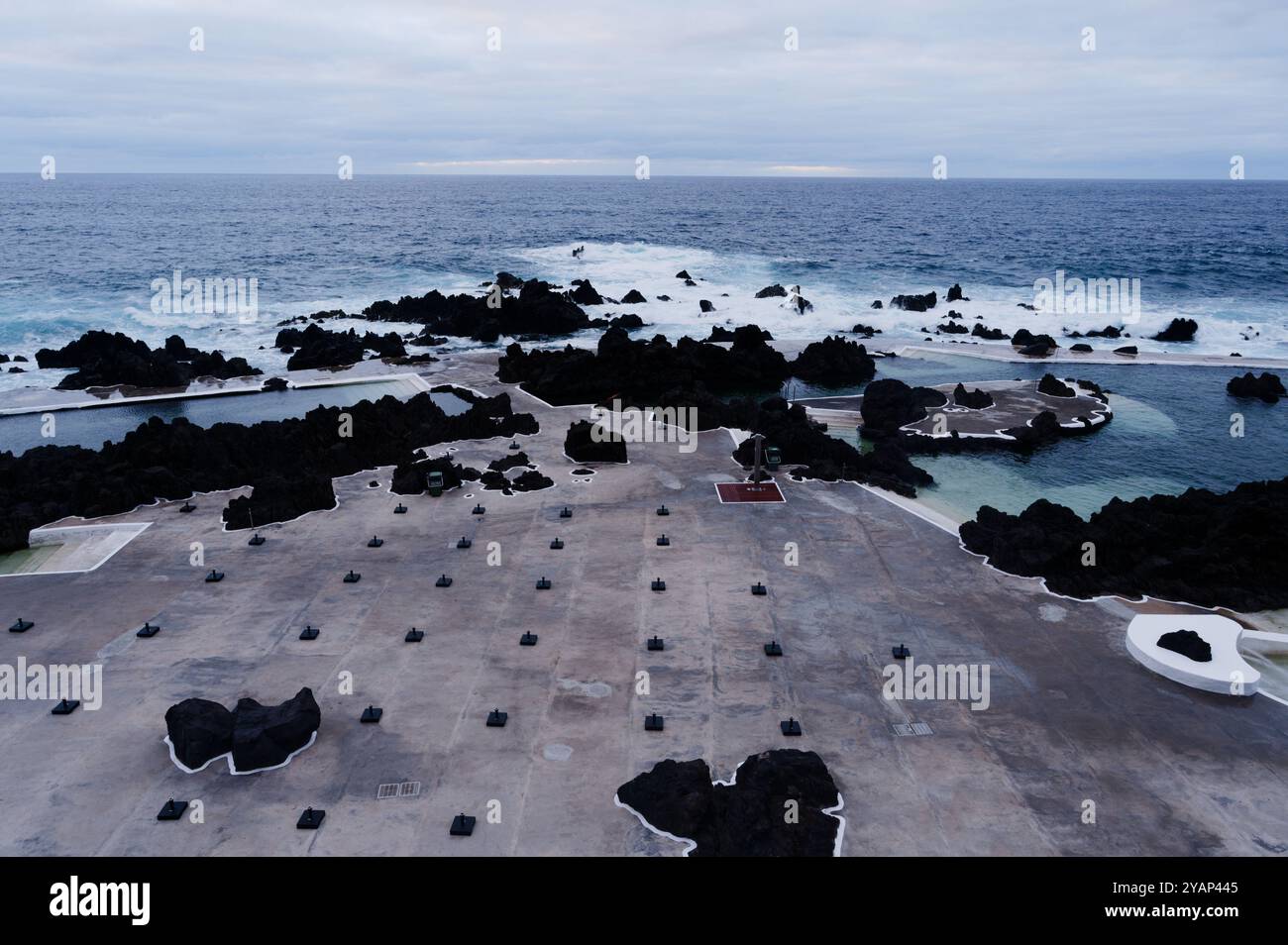 L'ombrellone vuoto si erge su cemento con rocce vulcaniche e onde che si infrangono nelle piscine naturali di Porto Moniz Foto Stock