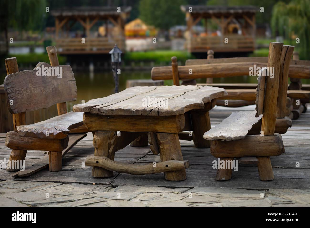 Panca rustica in legno e tavolo adagiati sul patio sul lago in un parco tranquillo in una giornata tranquilla Foto Stock