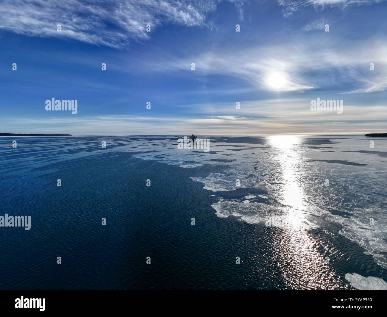 Nave da carico molto lontana nell'orizzonte in un luminoso, soleggiato e limpido giorno invernale in un mare calmo e semi-congelato blu scuro Foto Stock
