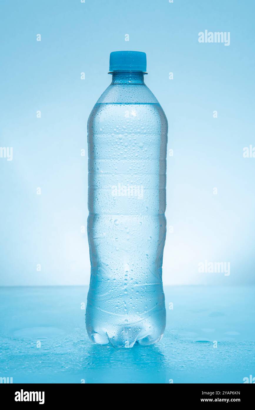 Flacone in plastica con coperchio smerigliato riempito d'acqua su una superficie blu riflettente bagnata su sfondo blu Foto Stock