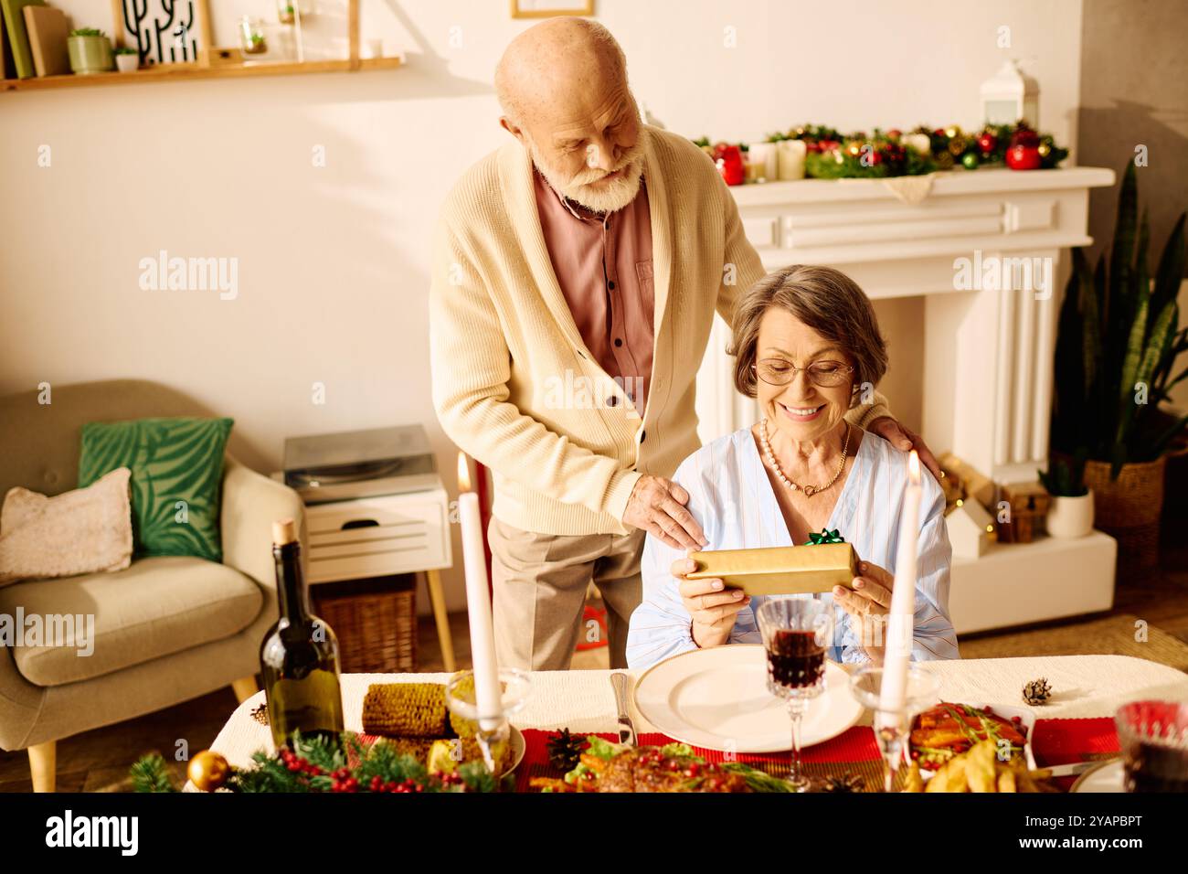 Una coppia anziana amorevole gode di un Natale natalizio a casa, aprendo regali e sorridendo. Foto Stock