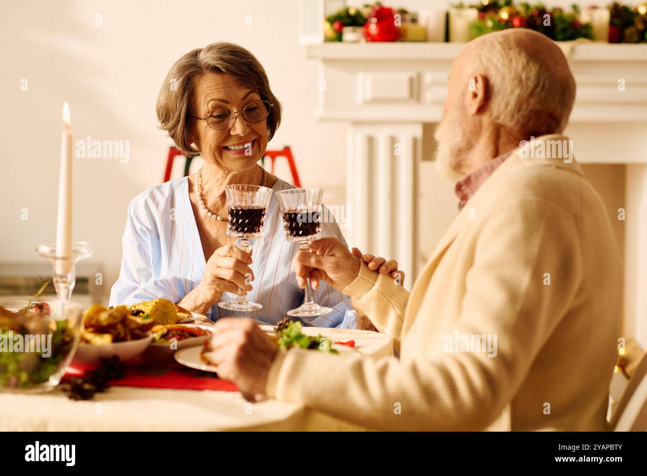 Una coppia anziana si diverte con un pasto natalizio festivo, brindando all'amore e all'amicizia. Foto Stock