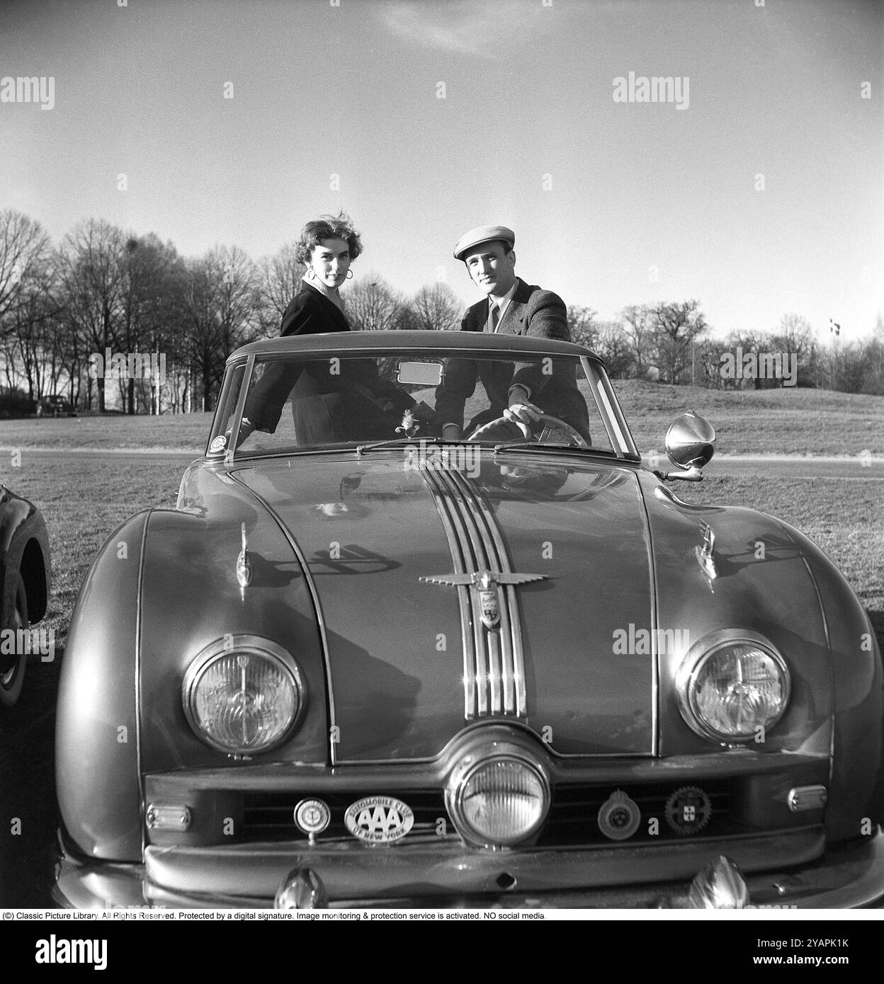 Un orgoglioso proprietario di auto negli anni '1950 Un uomo con la sua ragazza nella sua auto, un Austin del 1950 Un Atlantic del 90 con numero di registrazione A51517. L'auto è stata prodotta dalla casa automobilistica britannica Austin. Il modello era originariamente destinato ad essere venduto sul mercato americano. Aveva un corpo aperto, una convertibile. La vettura aveva un motore a benzina a 4 cilindri, 4 marce e trazione posteriore. L'auto aveva tre fari. Questo proprietario di auto era membro di associazioni automobilistiche internazionali, club automobilistici e i loro emblemi sono montati sulla parte anteriore dell'auto. Anders Svahn rif. SVA13 Foto Stock