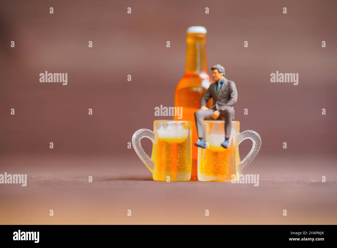 Scena creativa con un uomo d'affari in miniatura seduto su tazze da birra con una bottiglia dietro, che mette in risalto temi di svago ed equilibrio. Foto Stock