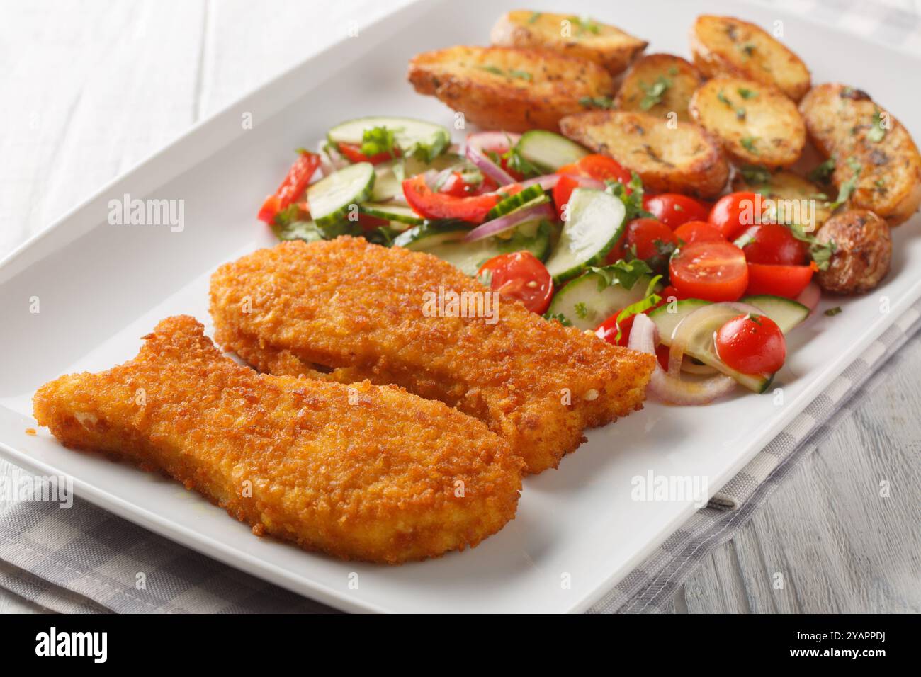 Pesce impanato fresco croccante con patate e insalata di verdure fresche primo piano in un piatto su un tavolo di legno. Orizzontale Foto Stock