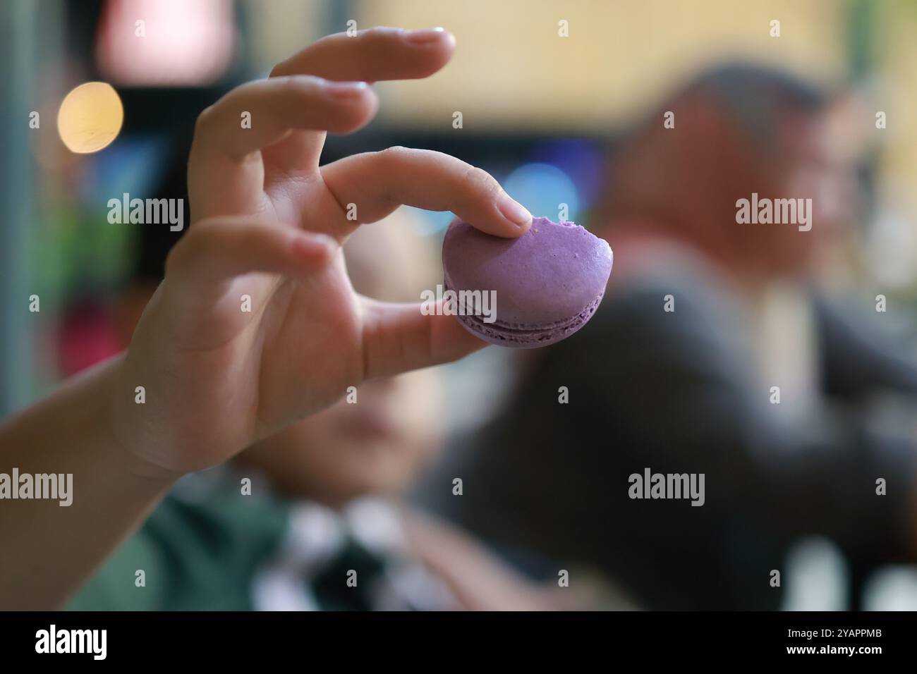 Primo piano dettagliato di una mano che presenta un delicato macaron viola, con uno sfondo sfocato che aggiunge profondità. Foto Stock