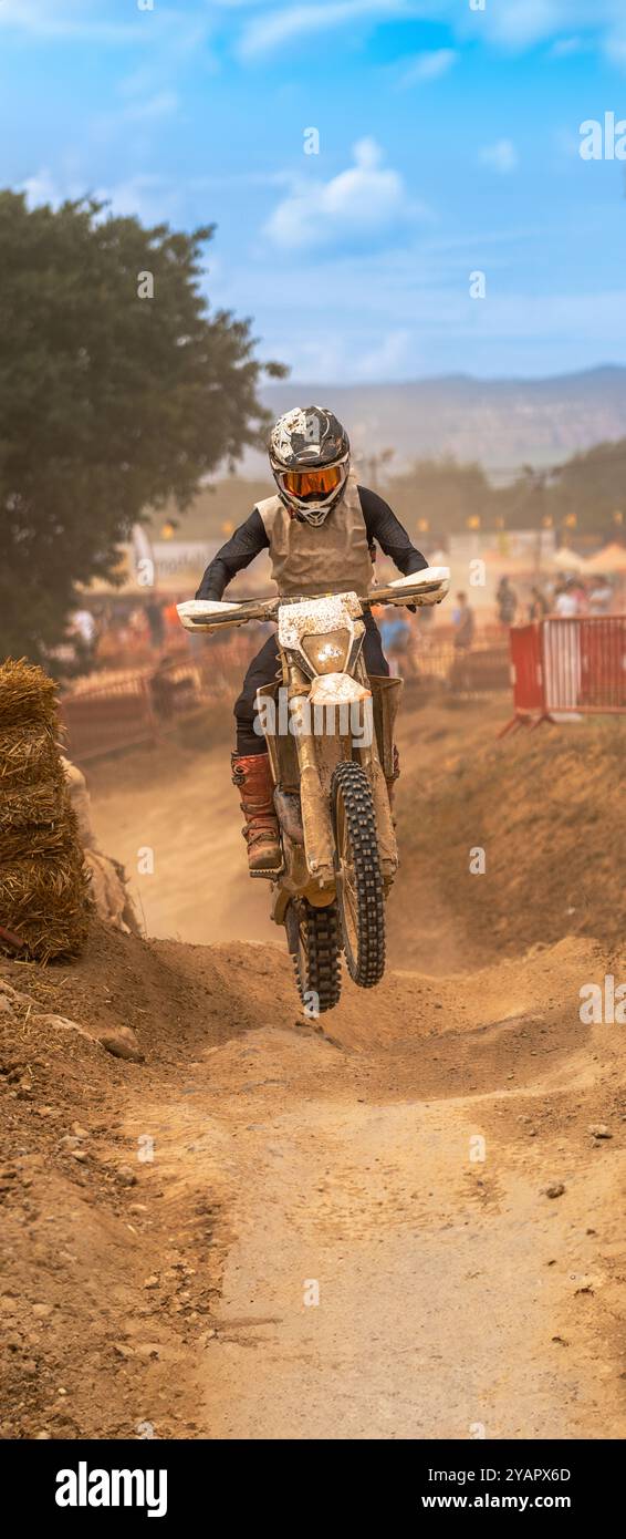 Donna in sella a una moto da motocross coperta di fango e polvere che salta con la propria moto durante il cambio di pendenza su una pista sterrata durante l'esterno sul monte Foto Stock