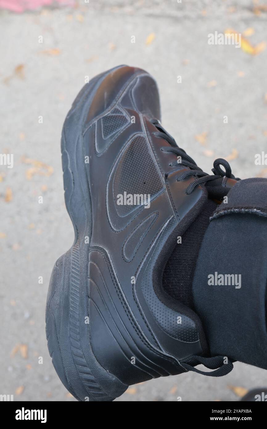 Primo piano di una scarpa sportiva nera su un fondo grigio con foglie gialle sparse. Foto Stock