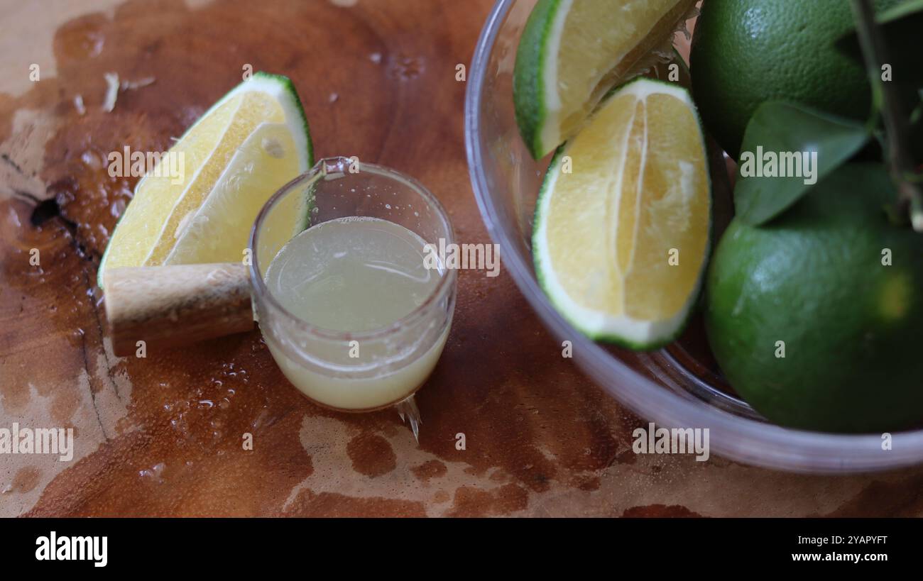 Fette di lime fresche e succo su una superficie rustica in legno Foto Stock